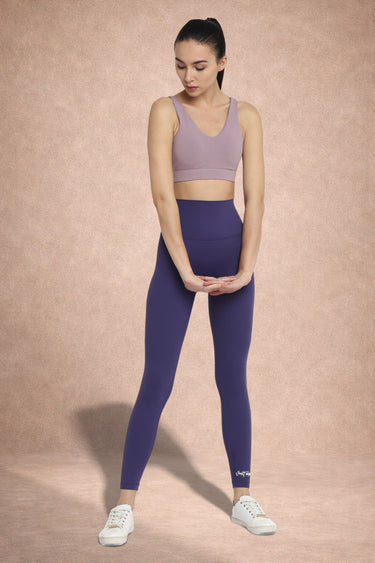 Woman wearing a purple sports bra and leggings on a beige background