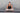 Woman performing a yoga pose on a mat with a gray brick wall background