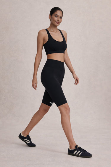 Woman wearing a Shakti Warrior black athletic outfit with shoes on a neutral background