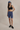 Woman wearing a black sports bra and blue shorts with a cap on a beige background
