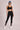 Person wearing a black sports bra and black lace leggings against a neutral background