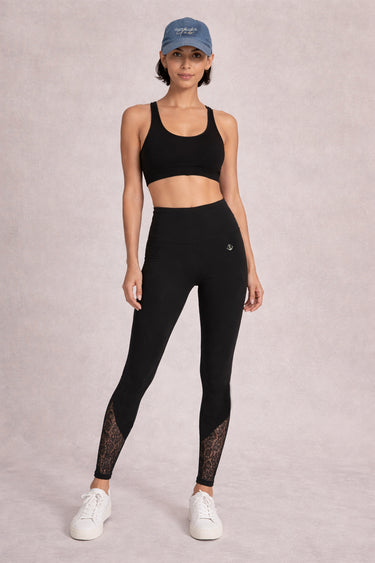 Person wearing a black sports bra and black lace leggings against a neutral background
