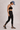 Person wearing a black sports bra and black lace leggings against a neutral background