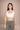 Woman wearing a white sports bra and green leggings against a beige background