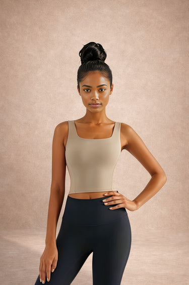 Woman wearing a beige sports bra and black leggings against a beige background