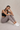 Woman wearing a black sports bra and gray leggings sitting on a beige background