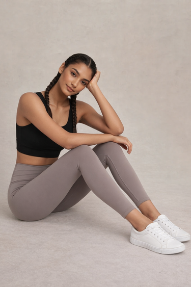 Woman wearing a black sports bra and gray leggings sitting on a beige background