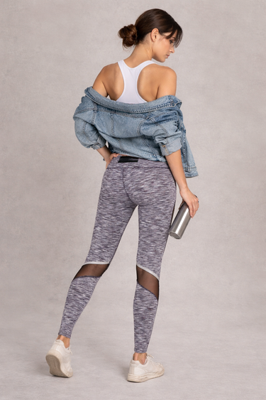 Woman wearing gray leggings and a white top with a denim jacket, standing against a plain background.