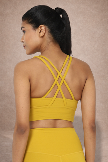 Woman wearing a yellow sports bra and leggings. The bra has a criss cross pattern giving high support