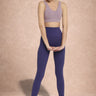 Woman wearing a purple sports bra and leggings on a beige background