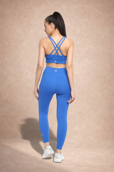 Woman wearing a blue sports bra and leggings set on a beige background