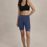 Woman wearing a black sports bra and blue shorts with a cap on a beige background