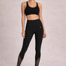 Person wearing a black sports bra and black lace leggings against a neutral background