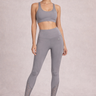 Person wearing a gray sports bra and gray lace leggings against a neutral background