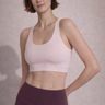 Woman wearing a light pink sports bra and maroon leggings against a neutral background