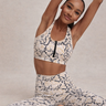 Woman in a animal print sports bra and matching leggings stretching against a neutral background