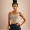 Woman wearing a beige sports bra and black leggings against a beige background