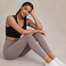 Woman wearing a black sports bra and gray leggings sitting on a beige background