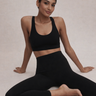Woman in black athletic wear sitting on a light gray background