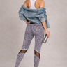Woman wearing gray leggings and a white top with a denim jacket, standing against a plain background.