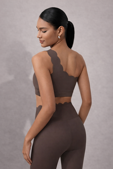 Shakti Warrior brown one-shoulder scallop detail sports bra and scallop detail leggings against a beige background