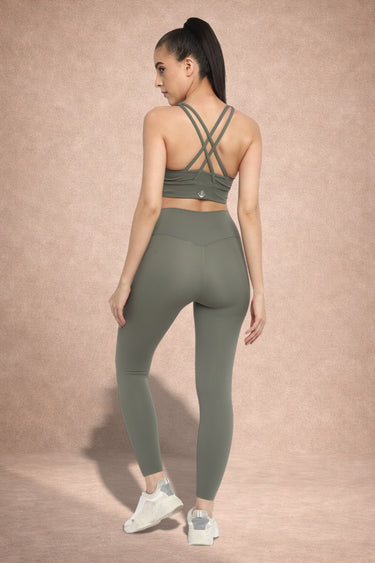 Woman wearing a green athletic outfit with criss-cross straps on a beige background